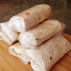 some food wrapped in plastic sitting on top of a wooden cutting board