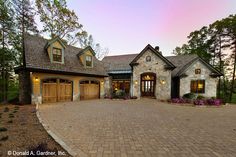 a large brick driveway leading to a stone house with two garages on each side