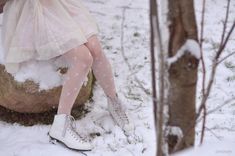 a woman sitting on top of a rock in the snow next to a tree trunk