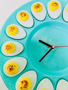 a clock made out of hard boiled eggs on a blue plate with black hands and feet