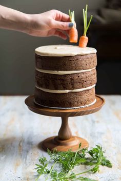 a person is placing carrots on top of a chocolate cake with icing and fresh herbs