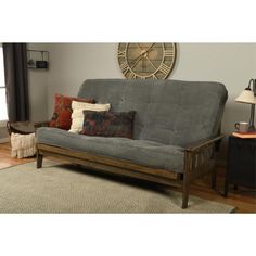 a living room with a futon and pillows on top of the couch, in front of a clock