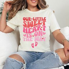 a woman wearing a t - shirt that says our little sweet heart is on the way