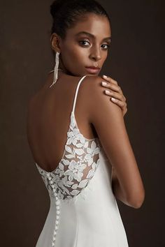 a woman in a white wedding dress posing for the camera with her hand on her shoulder