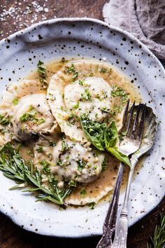 a white plate topped with dumplings covered in gravy and garnished with herbs