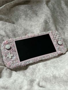 a pink nintendo wii game controller laying on top of a white bed sheet covered in beads