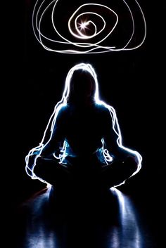 a woman sitting in the middle of a dark room with light painting on her face