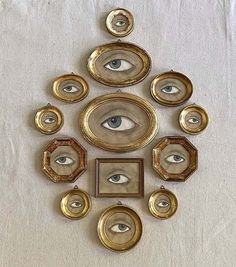 an eye is surrounded by gold frames and other decorative objects on a white cloth background