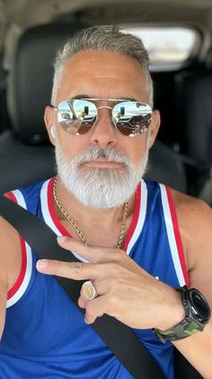 an older man wearing sunglasses and pointing to the side while sitting in a car seat