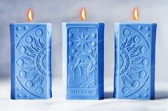 three blue candles sitting next to each other on top of a white surface with two lit candles