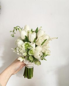 a bouquet of white tulips and other flowers is held up by a woman's hand