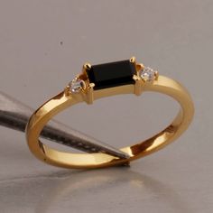 a gold ring with two diamonds and a black onyx stone in the center, sitting next to a pair of scissors