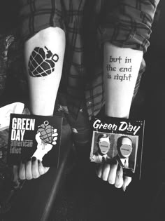 two people with tattoos on their arms holding up signs and posters that say green day