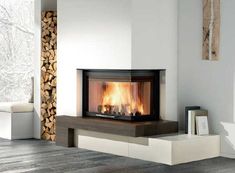 a modern fireplace in a living room with wood stacked on the floor and logs burning inside