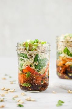 two mason jars filled with salads on top of a white countertop next to each other