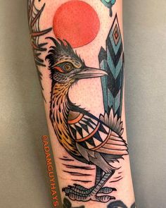 a bird tattoo on the leg with an orange ball in it's beak and feathers around its neck