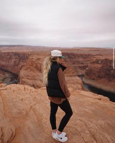 a woman standing on the edge of a cliff looking out at canyons and cliffs