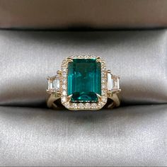 an emerald and diamond ring with three baguets on it's sides, sitting on a satin surface