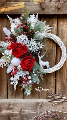 a wreath with red roses, white and green flowers is hanging on the side of a wooden wall