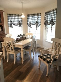 a dining room table with four chairs and a bench in front of two windows that have checkered valances on them