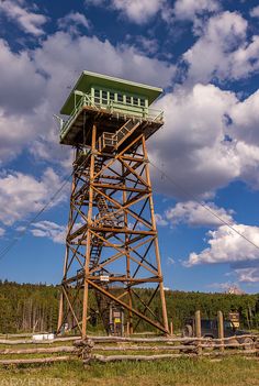 a tall wooden tower sitting on top of a lush green field under a cloudy blue sky