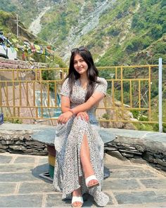 a woman sitting on top of a stone floor next to a mountain side area with mountains in the background