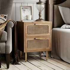 a nightstand with two drawers and a lamp on top of it next to a chair