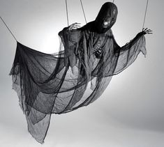 a black and white photo of a person in a ghost costume hanging on strings with the sun behind them