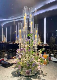 a vase filled with candles and flowers on top of a table next to other tables