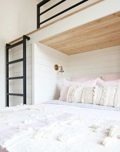 a bed with white sheets and pillows under a wooden headboard in a loft bedroom