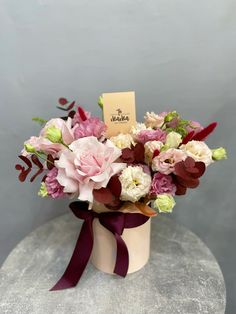 a bouquet of flowers in a vase with a name tag on the top and purple ribbon around it