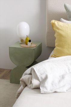 a green table with a white lamp on it next to a yellow pillow and bed