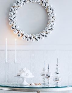 a white table topped with a glass top covered in pearls and candles next to a wreath