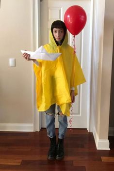 a person wearing a yellow raincoat and holding a red balloon in their hand while standing on a wooden floor