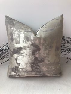 a silver pillow sitting on top of a white bed next to a branch filled wall