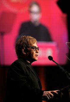 a woman standing at a podium in front of a screen with a man on it