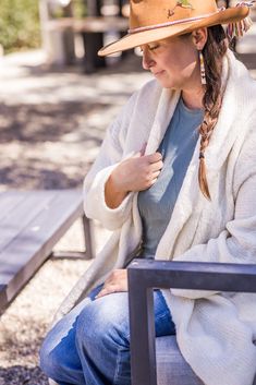 a woman sitting on a bench wearing a cowboy hat and holding her hand up to her chest