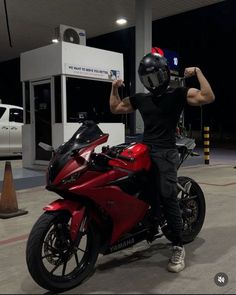 a man sitting on a red motorcycle in front of a gas station with his helmet on