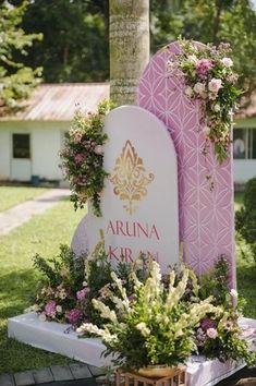 a pink and white grave marker with flowers on the top, surrounded by greenery