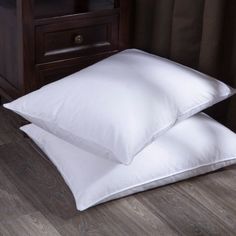 two white pillows sitting next to each other on top of a wooden floor in front of a night stand