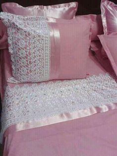 a bed with pink sheets and white lace on the pillowcase, along with matching pillows