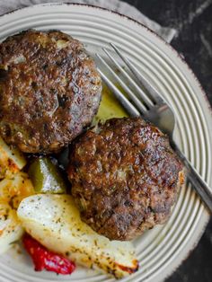 two hamburger patties with pickles and potatoes on a plate next to a fork