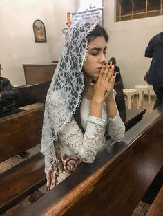 a woman sitting in a church with her hands clasped to her face and wearing a veil over her head