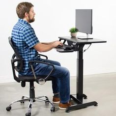 a man sitting at a computer desk with a plant on top of the monitor screen