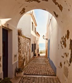 an alley way with cobblestone and blue doors leading to the water in the distance