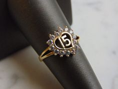 A WOMENS VINTAGE ESTATE 14K GOLD, LA QUINCEANERA HEART RING. THE RING IS A SIZE 6.75 AND WEIGHS 2.4g. THE STONES ARE EITHER CUBIC ZIRCONIA OR CRYSTALS. THIS IS A LOVELY GIFT FOR A YOUNG WOMAN TURNING 15 YEARS OF AGE. ANY QUESTIONS PLEASE DONT HESITATE TO ASK. BE SURE TO CHECK OUT SOME OF MY OTHER GREAT ITEMS UP FOR SALE. THANK YOU Round Engraved Ring With Hallmark For Anniversary, Oval Ring With Hallmark For Anniversary, Antique Gold Cluster Ring For Anniversary, 14k Gold Anniversary Birthstone Ring, Fine Jewelry 14k Stamped Birthstone Ring For Anniversary, 14k Stamped Birthstone Ring For Anniversary, Heirloom Yellow Gold Cluster Ring For Anniversary, Vintage 14k Gold Birthstone Ring For Anniversary, Vintage Gold Cluster Ring For Anniversary