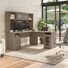 a computer desk sitting in front of a window next to a white chair and table