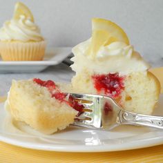 a piece of cake on a plate with a fork and cupcake in the background