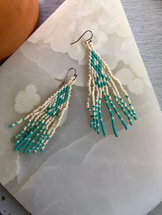 a pair of beaded earrings sitting on top of a white piece of paper next to a potted plant