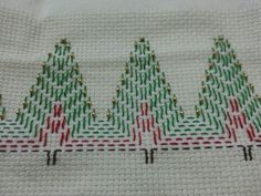 a cross - stitch christmas tree is shown in red, green and gold thread on a white cloth